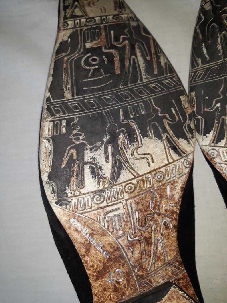 Puede incluir: Primer plano de la suela de un zapato de ante negro con un dise&ntilde;o detallado de una civilizaci&oacute;n antigua. El zapato es talla 40 y tiene el texto "Made in Italy" en la suela.