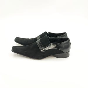 Puede incluir: Zapatos negros de ante con cordones, punta puntiaguda y ribete de cuero negro. Los zapatos tienen un tac&oacute;n bajo.