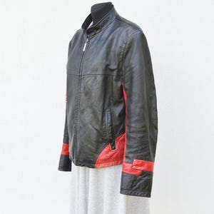 Puede incluir: Chaqueta de cuero negra con detalles rojos en las mangas y los lados. La chaqueta tiene cierre de cremallera y cuello alto.