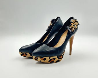 May include: Black platform heels with a leopard print sole and a bow detail. The heels have a wooden stiletto heel and a leather upper. The shoes are a stylish addition to any wardrobe.