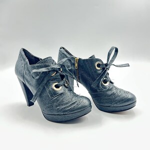 May include: A pair of black leather ankle boots with a high heel and platform sole. The boots feature a lace-up design with gold-tone eyelets and a side zipper. The leather has a textured finish.