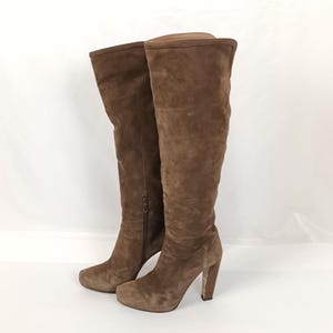 May include: A pair of knee-high brown suede boots. The boots have a rounded toe, a block heel, and a side zipper. The boots are a solid brown color and appear to be unworn.