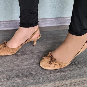 May include: A pair of light brown suede heeled sandals with a bow detail on the toe.
