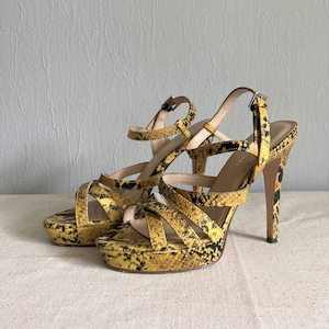 May include: A pair of yellow and black snakeskin platform sandals with high heels. The sandals have multiple straps and an open toe.