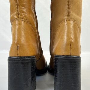 Puede incluir: Botas de cuero color canela con tacones de bloque negros. Las botas son de media ca&ntilde;a y tienen punta redonda. Los tacones miden aproximadamente 7,6 cm de alto. Las botas son de cuero liso.