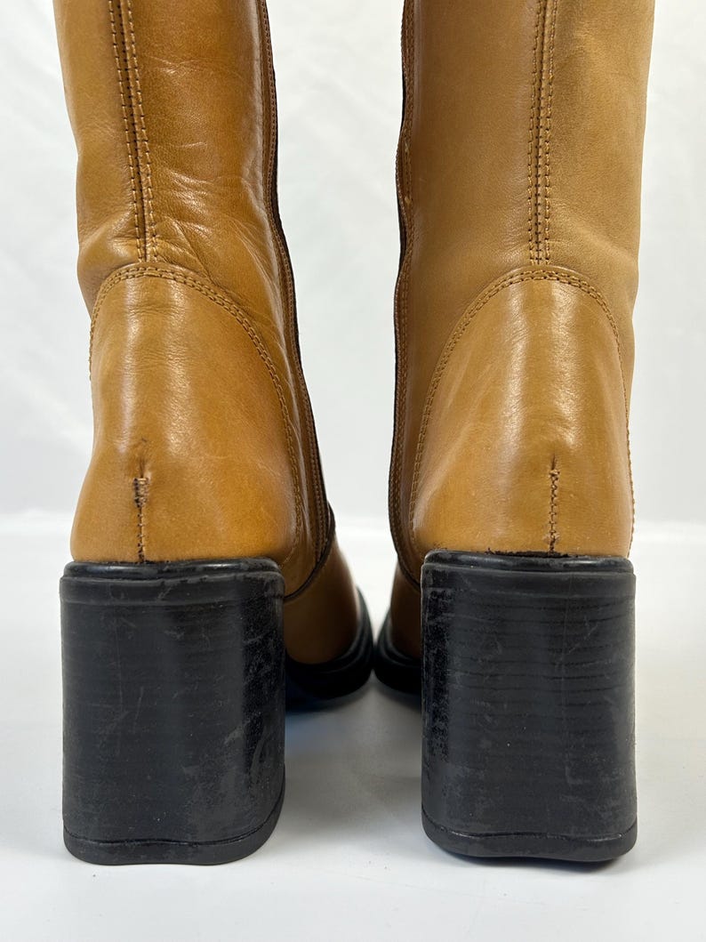 Puede incluir: Botas de cuero color canela con tacones de bloque negros. Las botas son de media ca&ntilde;a y tienen punta redonda. Los tacones miden aproximadamente 7,6 cm de alto. Las botas son de cuero liso.