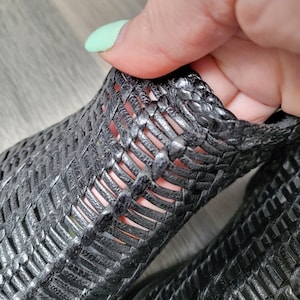 May include: Black woven leather ankle boots with a cut-out design. The boots are made of a soft, flexible material and have a comfortable fit.