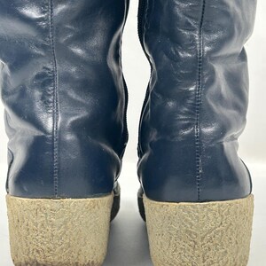 May include: A pair of navy blue leather boots with a textured, light brown sole. The boots have a tall shaft and a zipper on the side. The soles are approximately 2 inches thick.