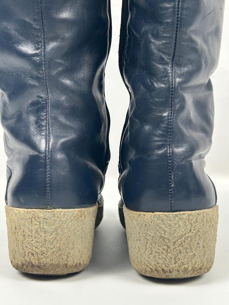 May include: A pair of navy blue leather boots with a textured, light brown sole. The boots have a tall shaft and a zipper on the side. The soles are approximately 2 inches thick.