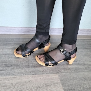 May include: A pair of black leather sandals with wooden heels. The sandals have a buckle closure and a strap across the foot.