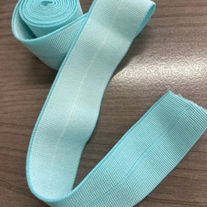Puede incluir: Un rollo de ribete el&aacute;stico azul claro con textura acanalada. El ribete tiene aproximadamente 2,5 cm de ancho.