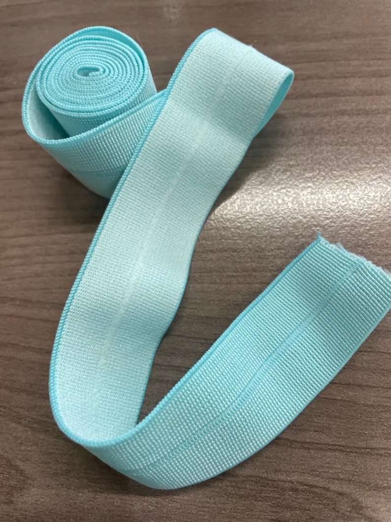 Puede incluir: Un rollo de ribete el&aacute;stico azul claro con textura acanalada. El ribete tiene aproximadamente 2,5 cm de ancho.