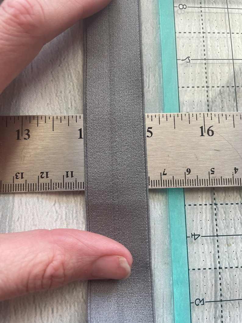 Puede incluir: Primer plano de una banda el&aacute;stica gris medida con una regla. La banda el&aacute;stica tiene 1,27 cm de ancho.