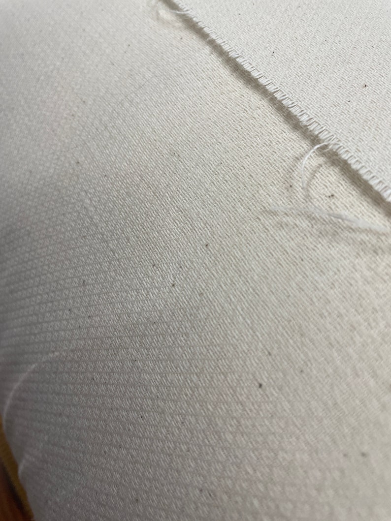 Puede incluir: Primer plano de una tela blanca con un sutil patr&oacute;n texturizado. La tela tiene un borde sin rematar y una costura que recorre la superficie en diagonal.