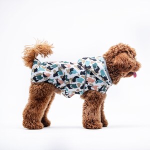 May include: A brown dog wearing a hooded camouflage raincoat with a white, blue, and green pattern.