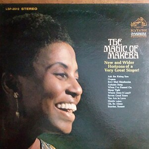 May include: A vintage vinyl record album cover featuring a close-up portrait of a woman with a warm smile. The album title is "The Magic of Makeba" with the subtitle "New and Wider Horizons of a Very Great Singer!" The album cover is black with white text.
