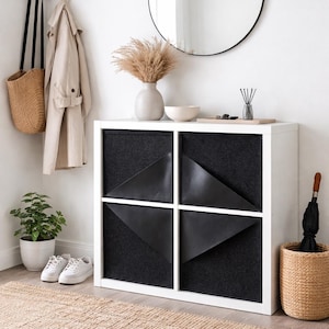 Puede incluir: Una entrada moderna con una unidad de almacenamiento blanca con detalles geométricos negros. Un espejo redondo cuelga encima, con un perchero, una cesta de mimbre y una alfombra beige. Una planta en maceta y zapatillas añaden un toque de vegetación y estilo casual.