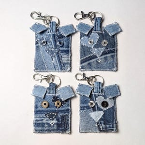 May include: Four rectangular keychains crafted from blue denim fabric scraps. Each piece features stitched denim ears, button eyes, and a fabric nose. The designs include heart-shaped patches and white decorative stitching, all attached to silver metal clasps.