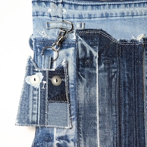 May include: A denim fabric accessory featuring a cat-shaped charm attached with a silver metal lobster clasp. The charm is constructed from patchwork denim scraps in various blue shades, accented with two round buttons for eyes and white stitching.