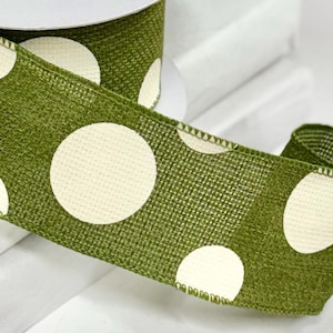 May include: A roll of olive green ribbon with large, cream-colored polka dots. The ribbon is made of a textured fabric and is partially unrolled, revealing the white cardboard spool. This decorative ribbon is suitable for crafts and gift wrapping.