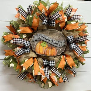 May include: A fall-themed wreath with orange, green, and black and white checkered ribbon. The wreath has a wooden sign that says "Welcome Friends".