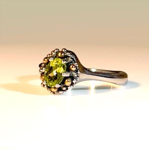 Può includere: Un anello d'argento con una pietra preziosa verde incastonata in un design a corona d'oro e argento.