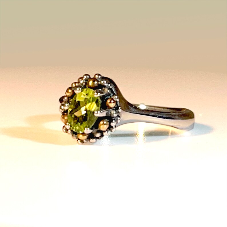 May include: A silver ring featuring a green gemstone set within a gold and silver crown design.