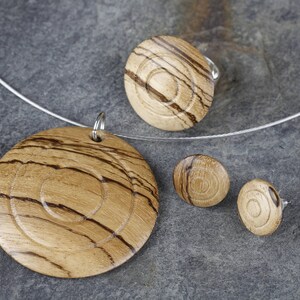 May include: A set of wooden jewelry featuring a necklace, a ring, and earrings. The jewelry is made of light brown wood with dark brown stripes. The pieces are all circular in shape and have a concentric circle design.