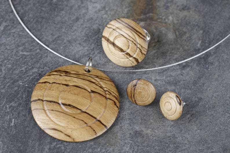 May include: A set of wooden jewelry featuring a necklace, a ring, and earrings. The jewelry is made of light brown wood with dark brown stripes. The pieces are all circular in shape and have a concentric circle design.