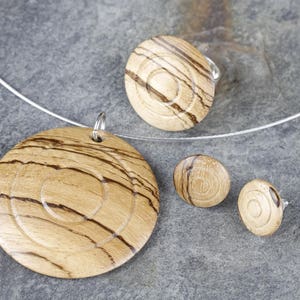 May include: A wooden jewelry set with a necklace, ring, and earrings. The pieces are all made of light brown wood with a swirling grain pattern.