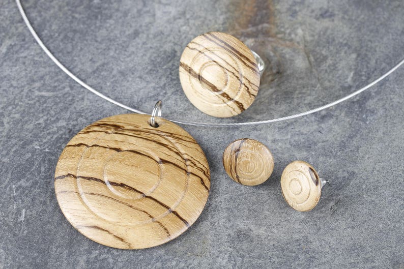 May include: A wooden jewelry set with a necklace, ring, and earrings. The pieces are all made of light brown wood with a swirling grain pattern.