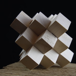 Könnte beinhalten: Ein weißes Holzpuzzle aus ineinandergreifenden Würfeln. Das Puzzle hat die Form eines Würfels und liegt auf einem Stück verwittertem Holz.