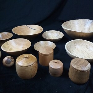 May include: A collection of wooden bowls and containers of various sizes and shapes. The bowls are made of light wood with a natural grain pattern. The containers have lids and are also made of light wood.