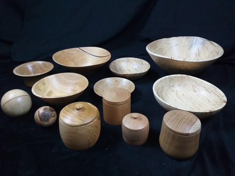 May include: A collection of wooden bowls and containers of various sizes and shapes. The bowls are made of light wood with a natural grain pattern. The containers have lids and are also made of light wood.