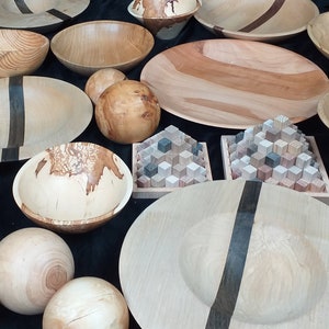 May include: A collection of wooden bowls and spheres, some with dark wood accents, displayed on a black surface. The bowls are various sizes and shapes, with some featuring a natural wood grain pattern.