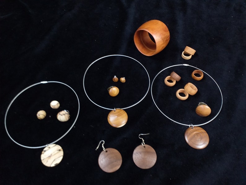 May include: A set of wooden jewelry featuring necklaces, earrings, and rings. The jewelry is made from different types of wood, each with its own unique grain pattern. The pieces are all natural and have a warm, earthy tone.