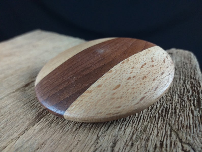 May include: A round wooden coaster with a light brown and dark brown wood grain pattern. The coaster is made of two different types of wood.