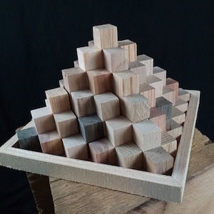 Könnte beinhalten: Eine Holzpyramide aus kleinen, quadratischen Blöcken, die in einer dreieckigen Form angeordnet sind, steht auf einer Holzbasis. Die Blöcke sind aus verschiedenen Holzarten gefertigt, wodurch eine Vielzahl von Farben und Texturen entsteht.