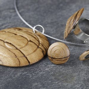 May include: A set of wooden jewelry featuring a pendant, a ring, and a pair of earrings. The jewelry is made of light brown wood with dark brown streaks. The ring has a silver band.