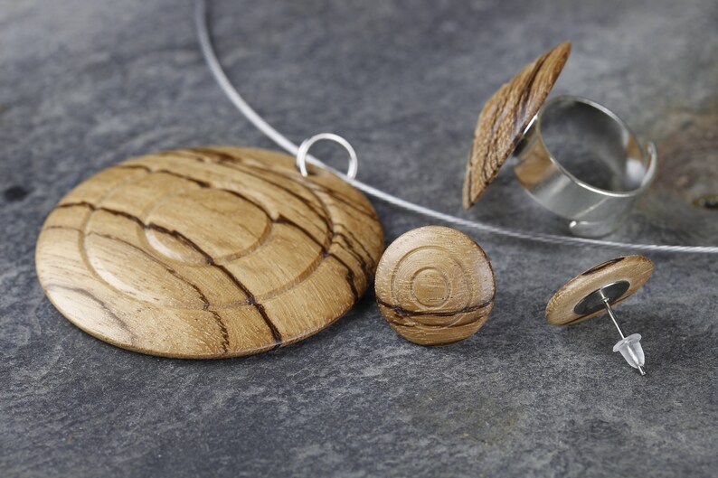 May include: A set of wooden jewelry featuring a pendant, a ring, and a pair of earrings. The jewelry is made of light brown wood with dark brown streaks. The ring has a silver band.