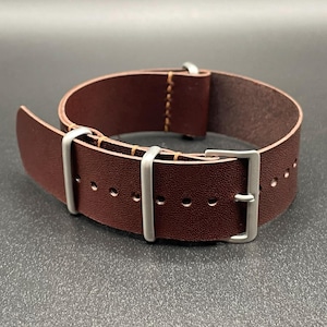 May include: A brown leather watch strap with silver-colored hardware. The strap has a buckle closure and multiple adjustment holes. The leather appears to be textured, and the stitching is visible.