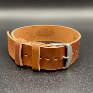 May include: A light brown leather watch strap with a silver-colored buckle. The strap is made of thick leather and has a classic design. The brand name "HORWEEN" is stamped on the inside of the strap.
