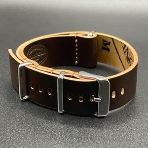 May include: A dark brown leather watch strap with a silver buckle and keepers. The strap has a light brown interior and is stitched with light brown thread. The strap is approximately 9 inches long.