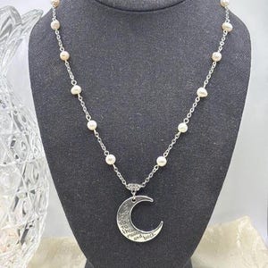 May include: A silver-toned necklace with a crescent moon pendant. The necklace features a chain interspersed with small pearls. The moon pendant has the inscription "I love you to the moon and back."