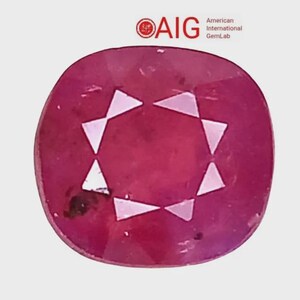 May include: A cushion-cut ruby gemstone with a deep red hue and a faceted surface. The stone features a central star-like pattern of light reflections. The AIG American International GemLab logo is visible in the upper right corner.
