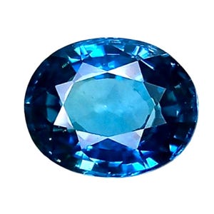 May include: Oval-cut gemstone with a brilliant, faceted design. The gem features a gradient of blue hues, transitioning from a lighter center to a deeper, darker blue around the edges. The gem is set against a white background.
