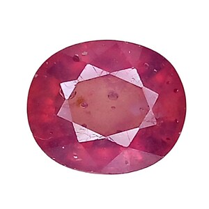 May include: A faceted oval-shaped gemstone with a deep pinkish-red hue. The stone features a central star-like pattern created by its cut, with visible internal inclusions and a polished surface that reflects light across its translucent body.