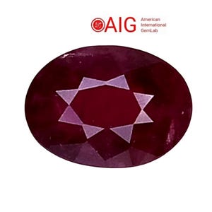 Può includere: Gemma ovale rosso scuro con un motivo a forma di stella al centro. La gemma è posta su uno sfondo bianco. L'immagine include il testo "AIG American International GemLab".