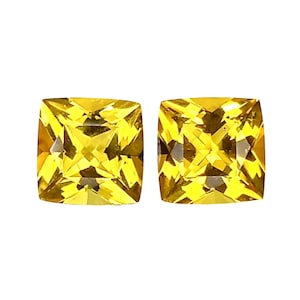 Puede incluir: Dos gemas amarillas cuadradas y facetadas. Las gemas tienen un tono dorado brillante y están sobre un fondo blanco. Las gemas son probablemente para la fabricación de joyas.