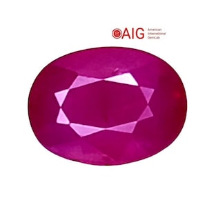 May include: An oval-cut, vibrant magenta-red gemstone with a faceted surface that reflects light. The stone is positioned below the red and black AIG American International GemLab logo, which is printed in the upper right corner of the frame.